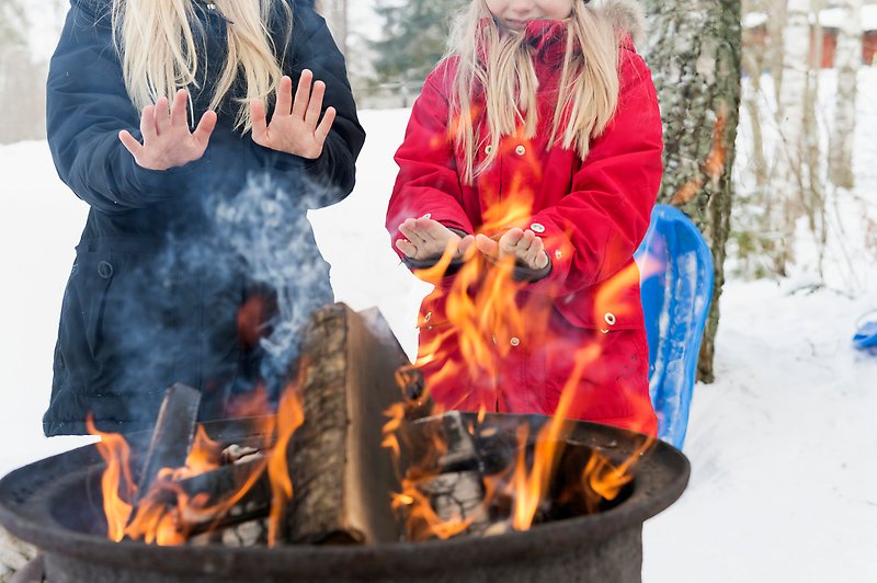 Två flickor värmer händerna vid en brasa i vintertid