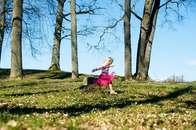 Ett barn springer i en skog med vårblommor på marken